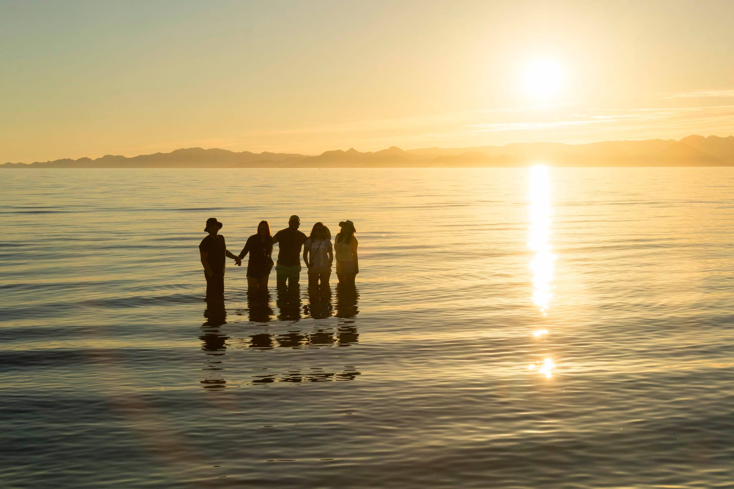 Grupo de viajeros en siluetas dentro del Mar de Cortés al amanecer